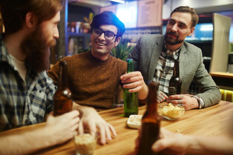 Three men smiling and enjoying beer together indoors. Perfect for themes of friendship and leisure.